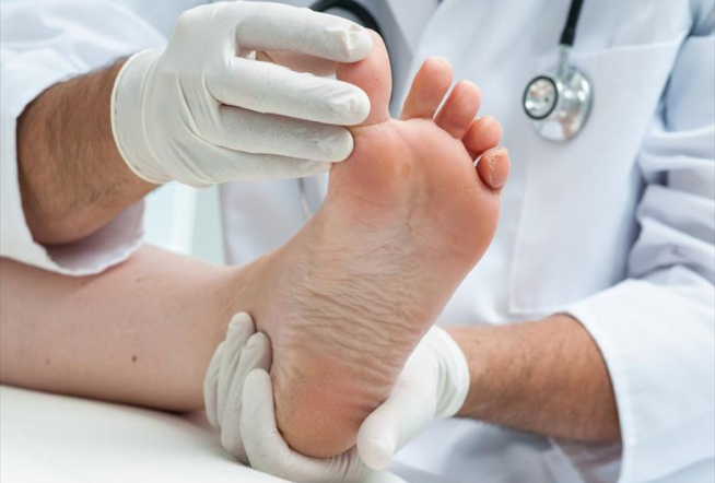 Doctor wearing gloves examining the bottom of a patient’s foot during podiatry checkup.